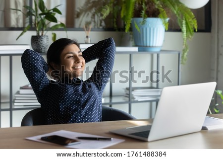 Carefree indian employee resting after busy fruitful workday leaned on office chair puts hands behind head feels satisfied by work done, achievements, job promotion, looking in distance out the window Royalty-Free Stock Photo #1761488384