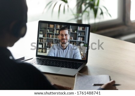Girl trainee learn language wear headphones view over her shoulder laptop screen where male tutor share knowledge smile looks at camera. Colleagues work distantly using video call and computer concept Royalty-Free Stock Photo #1761488741