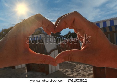 Heart out of hands against the sun with defocused beach chairs in the background at the beach of Binz, Germany.