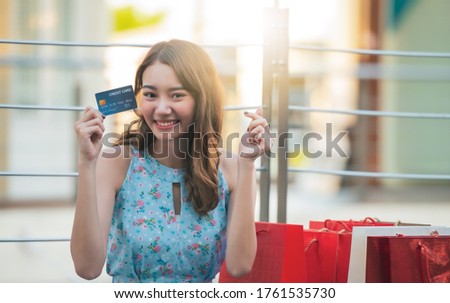 Young Asian shopping woman with shopping bags holding credit card and made little heart sign , shopping concept.