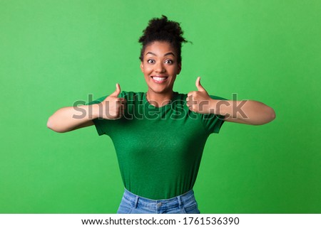 I Like It. Overjoyed black girl showing two thumbs up and widely smiling, isolated over green studio wall, copyspace