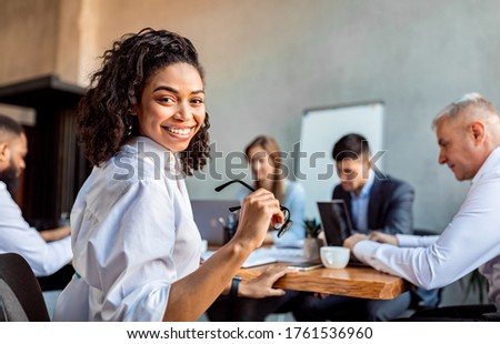 Cheerful African Businesswoman At Corporate Meeting Sitting With Business Partners Posing In Modern Office. Free Space