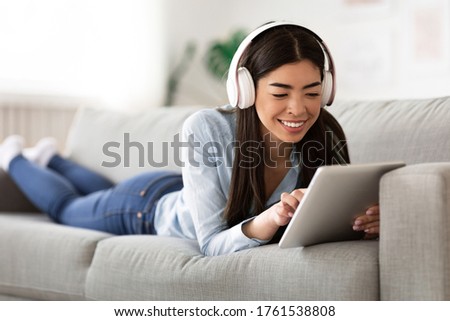 Favorite Leisure. Young Asian Girl Relaxing With Digital Tablet And Wireless Headphones On Couch At Home, Browsing Internet Or Listening Music