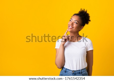 I Think. Dreamy african woman looking up, touching her chin with finger, isolated over yellow studio wall, copyspace
