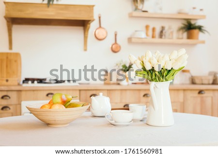 Breakfast cups and fruit. Spring tulips on the table. Wooden table in a bright rustic-style kitchen. Scandinavian style in the interior of the kitchen. Royalty-Free Stock Photo #1761560981