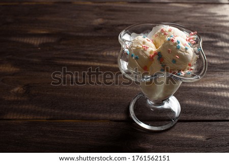 White balls of vanilla ice cream under colorful sprinkles in a dessert bowl. Decorated ice cream on a dark wood table.