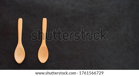 two wooden empty spoons on a dark slate background. top view. panoramic format with copy space for text