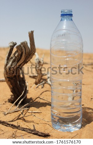 Plastic water bottle on hot and arid desert sand. Desert survival/plastic pollution concept.