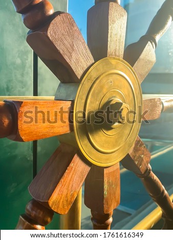 Authentic steering wheel of a ship, the helm mounted to a fence in bar interior. Old wooden rustic mood and texture, sun rays coming through the window. Navy template