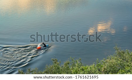 open water swimmer with a swim buoy on a calm lake, summer morning workout Royalty-Free Stock Photo #1761621695