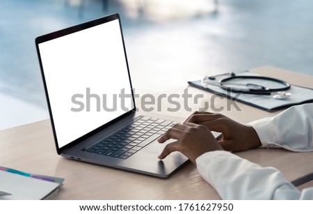 African american doctor wear white coat typing using laptop computer mock up white screen browsing internet sitting at work desk. Healthcare medical e health website technology concept. Close up view Royalty-Free Stock Photo #1761627950
