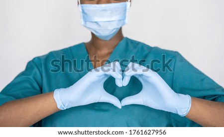 Female african professional medic nurse wear face mask, gloves, blue green uniform showing heart hands shape. Medical love, care and safety symbol, corona virus health protection sign concept. Closeup Royalty-Free Stock Photo #1761627956