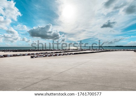 Wide cement road and lake under blue sky.