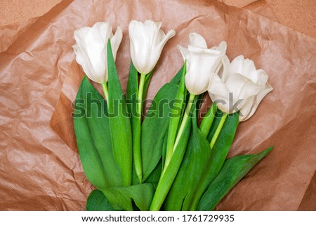 Bouquet of bright delicate white tulips with bright green foliage in craft paper on a background of wood plate