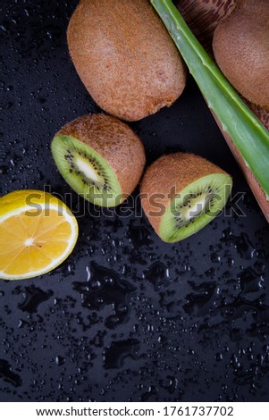 A close shot of chopped lemon, a full kiwi and an aloe vera leaf on a black background.