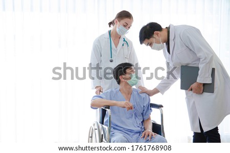 Doctors and patient wearing face mask protect from COVID-19 and flu outbreak in hospital room.Doctors empathy and encouragement patient sitting wheelchair to get better on white background.