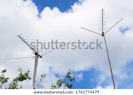 Two home TV antennas stand on long poles against the background of sky and clouds. Shot in summer in the countryside. Bright illustration on the theme of television and the media
