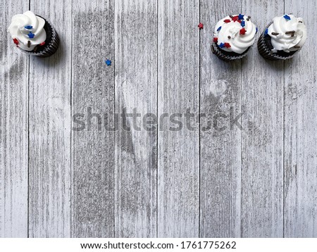 three white muffins, cupcakes with American-colored stars on a white rough wooden board stand at the top, background for text, free space for design high quality photo for USA Independence Day