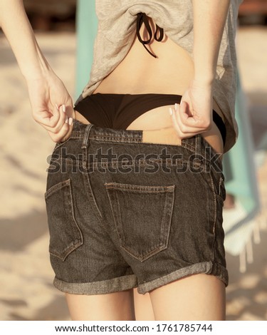 A girl in a bikini dresses shorts on the beach.