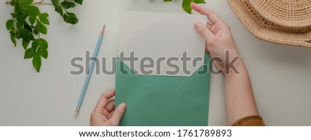 Overhead shot of female hands open mock-up greeting card with turquoise  envelope on table with pencil and decorations 