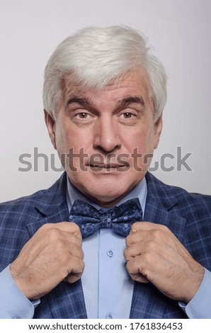 Portrait of a courageous and brutal, majestic, rich and mature man, scientist, financier, businessman with gray hair, in a checkered blue jacket, bow-tie or tie on a light and white background.
