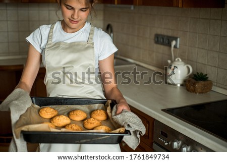 Smiling teen girl taking cookies out of the oven in the kitchen. Homemade cakes, cookies and gingerbread cookies. sweet breakfast.