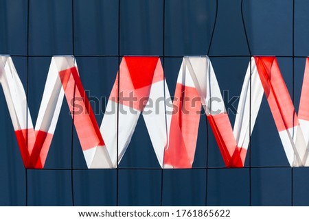 Barrier tape in red and white color on a hoarding construction fence forming letters M an W in a zick zack line. Transparent plastic tape acklit by sunlight: No entry, do not cross!