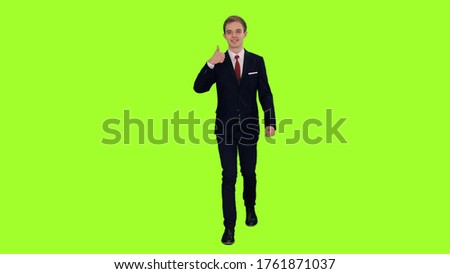 Young stylish man in suit showing thumb up sign while walking on green chroma key background, Front view