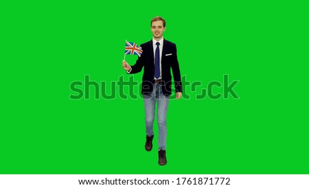 Young smiling business man in jacket suit and jeans walking with waving flag of UK on green screen background, chroma key 4k footage