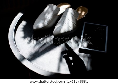 white shoes on a black background in the style for blogging, a finger indicates shoes, a hand shadow, a plate with an empty place for a price tag or inscription, casual leather shoes