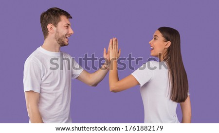 Image of friendly young people man and woman in basic clothing giving high five isolated over purple studio wall Royalty-Free Stock Photo #1761882179