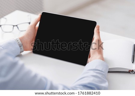 Workspace with tablet and businessman hands. Guy holding gadget with blank screen for an online consultation, on table are glasses and notebook