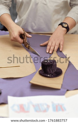 Workplace of seamstress. Dressmaker cuts textile on the sketch lines. female hand with the scissors cutting fabric.
