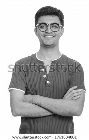 Portrait of happy young handsome Persian nerd man smiling with arms crossed