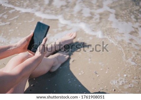 girl sitting on the sand near the sea with a phone in her hands
