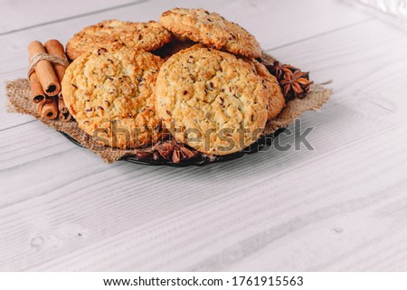  baked oatmeal cookie on plate with napkin decorated with cinnamon sticks, coffee and star anise on white wooden table background. Image use for commercial or menu layout design. Copy space.