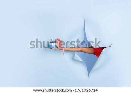 Female hand giving presents, gift, surprise in torn blue paper hole background. Breaking on, breakthrought. Concept of celebration, shopping, proposal, sales, ad. Copyspace. Promotions discounts