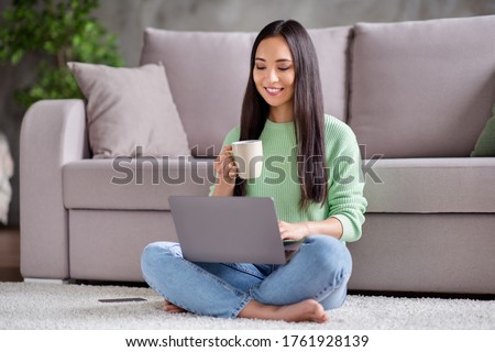 Full length photo of positive korean student girl sit floor legs crossed folded work remote laptop read document report hold mug beverage in house indoors