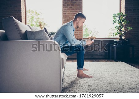 Profile photo of handsome barefoot guy stay home quarantine time hold telephone blogger freelancer good mood check likes followers sit comfy sofa modern interior living room indoors