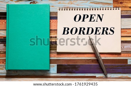 The text Open Border is written on a white sheet near a notebook and pen.