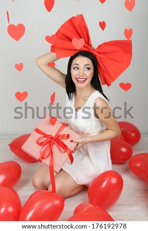 Attractive young woman with gift and balloons in room on Valentine Day