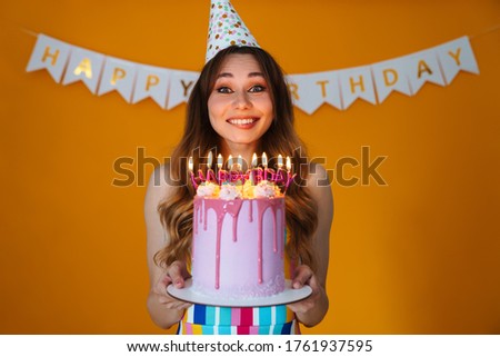 Image of delighted young woman in party cone showing birthday torte with candles isolated over yellow background