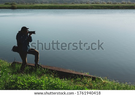 Young male photographer holding a camera in his hands near the river. Landscape photography. With a copy space.