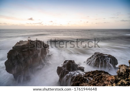 Rocks in Atlantic Ocean by sunset in Nazare, Portugal. Long exposure photography.