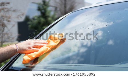 Hand wiping the windshield of a car on a sunny day. Wipe dry with an orange sponge. Rag wipes water stains on the window Royalty-Free Stock Photo #1761955892
