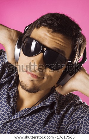 Young guy listening music with headphones, pink background
