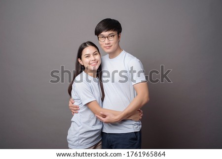 a portriat of a happy couple wearing blue shirt is hugging each other in grey background studio