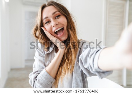 Cheerful attractive young woman taking a selfie while standing in the living room