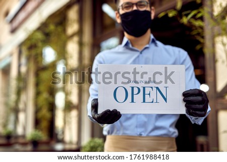Close-up of waiter holding open sign while reopening cafe after coronavirus pandemic. 