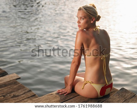 Young woman sitting on jetty looking over shoulder back view
